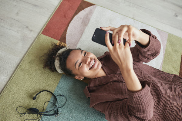 woman lays on carpet and smiles at phone